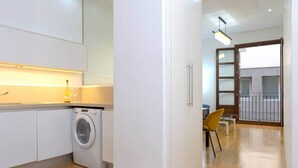 Une cuisine moderne équipée d’un lave-linge, un coin repas avec une table et des chaises, et un balcon avec une balustrade.