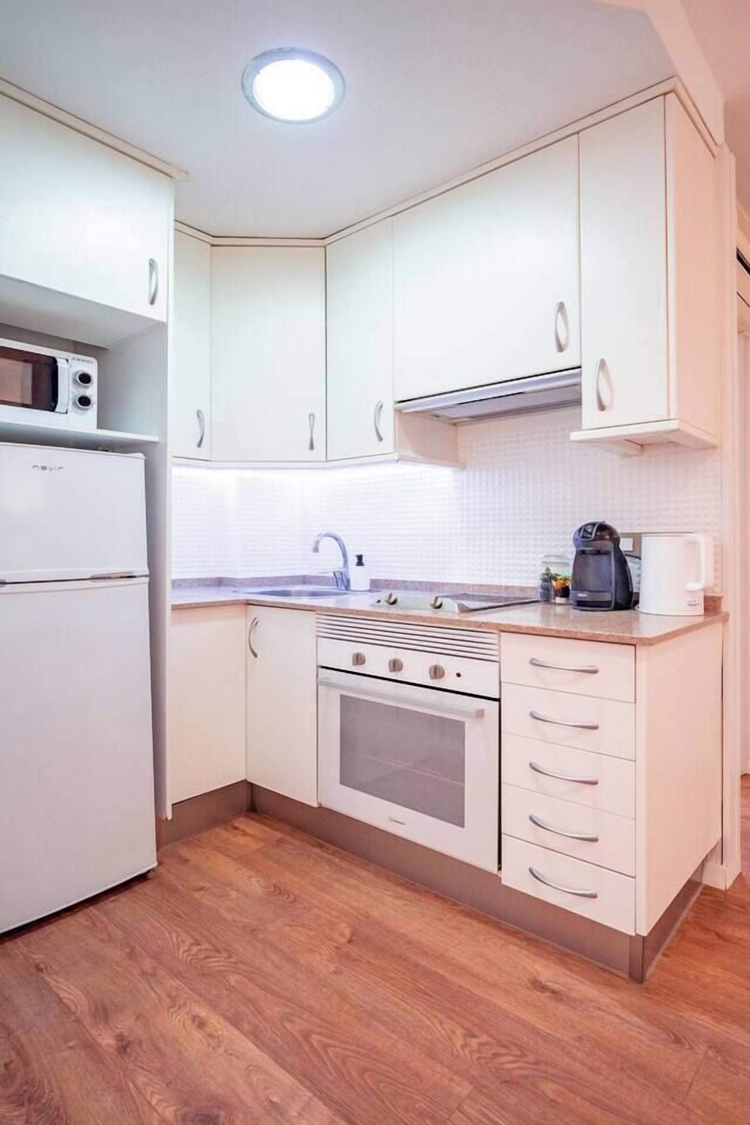 Une cuisine compacte avec des meubles blancs, un four encastré et un micro-ondes.