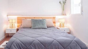 A bedroom with a large bed, two bedside tables with lamps, a wooden headboard, and a window with a plant. - Next to the Silk Exchange and Central Market (Valencia)