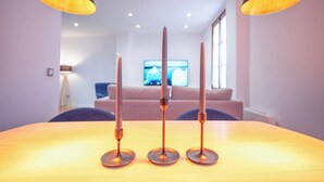 A dining table with three candles and two lamps in a modern room with a sofa and a TV in the background. - Next to the Silk Exchange and Central Market (Valencia)
