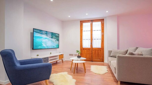 A modern living room with a flat-screen TV, a blue armchair, a grey sofa, a wooden coffee table, and a white rug. - Next to the Silk Exchange and Central Market (Valencia)