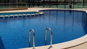 En swimmingpool med to metalstiger, omgivet af en flisbelagt terrasse og glasgelændere.