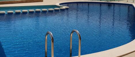 A swimming pool with two metal ladders, surrounded by a tiled deck and glass railings.