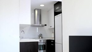 Et kompakt køkken med moderne hårde hvidevarer, indbygget ovn og et fladskærms TV på et stativ.