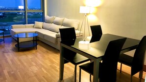 Een moderne woonkamer met een bank, een glazen salontafel, een eettafel met stoelen en een vloerlamp.