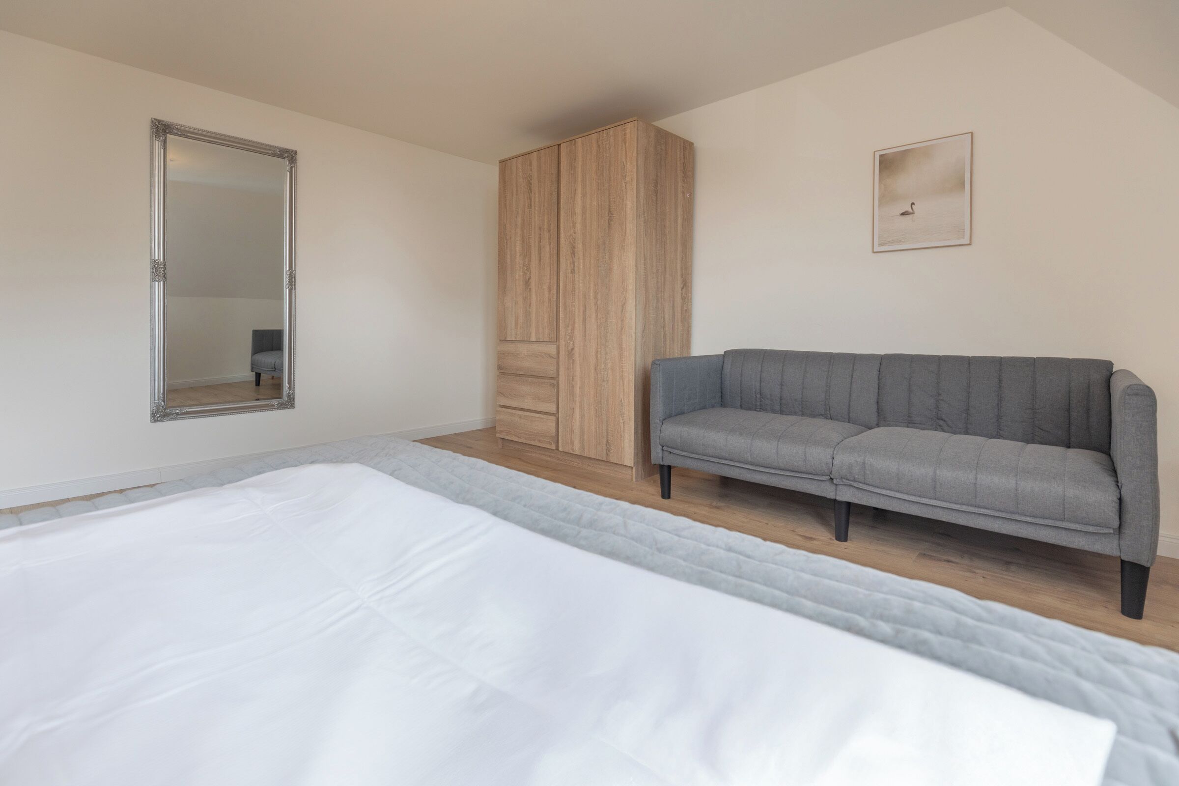 Une chambre à coucher avec un grand lit, un canapé gris, une armoire et un miroir.