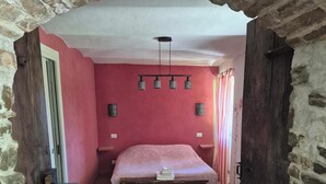 Un dormitorio con piso de ladrillo, una cama, un banco de madera y una pared de piedra.
