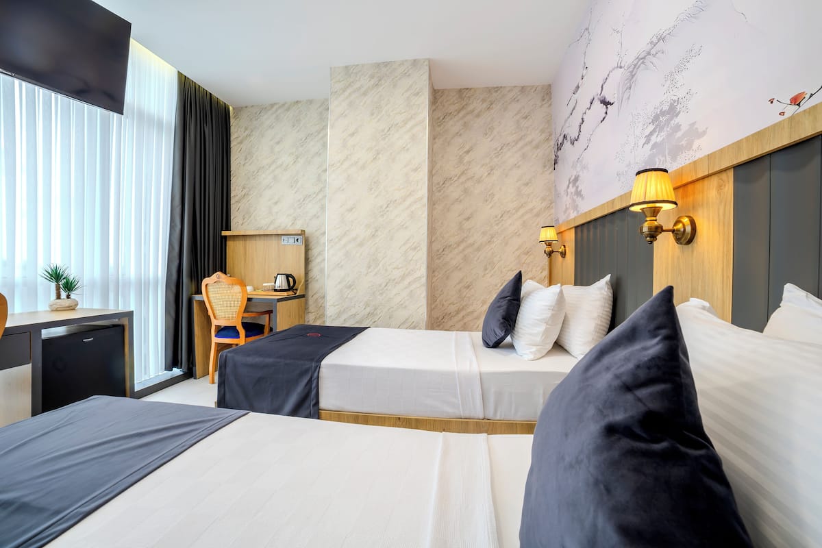 Ein Hotelzimmer mit zwei Betten, einem Schreibtisch, einem Stuhl und einer kleinen Küchenzeile.
