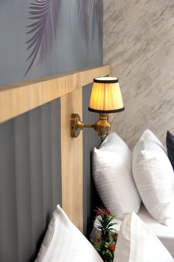 Una lámpara de pared con acabado de latón, cabecera de madera y almohadas blancas.