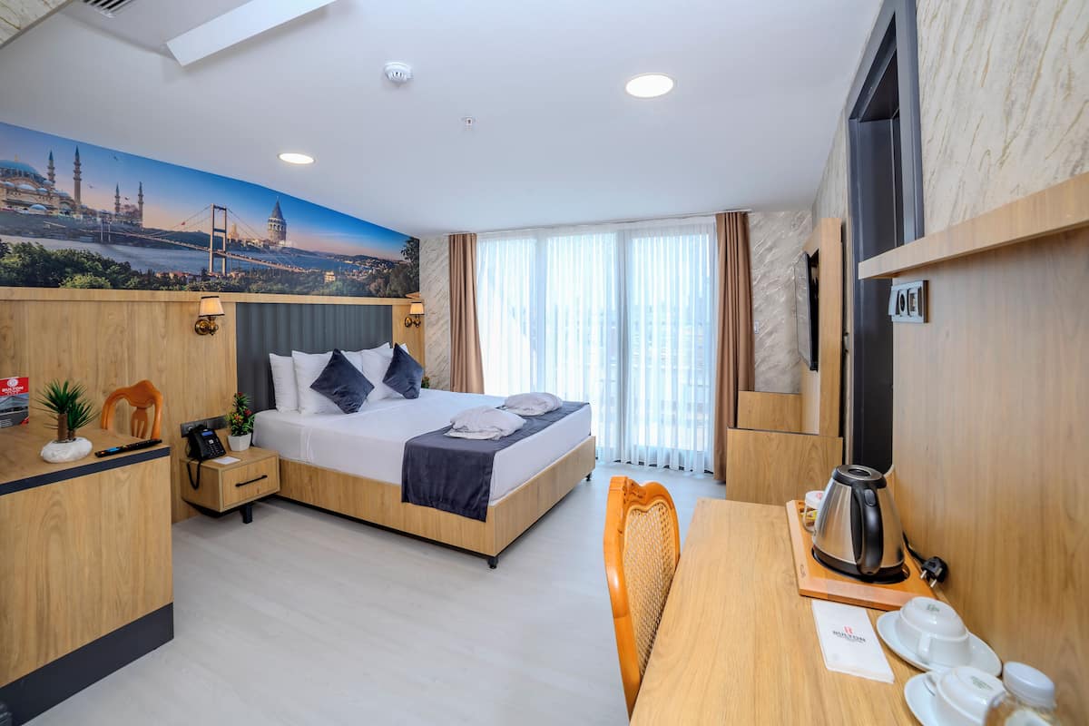 Ein modernes Hotelzimmer mit einem Bett, einem Schreibtisch mit Kaffeemaschine, einem Telefon und einem an der Wand montierten Fernseher.