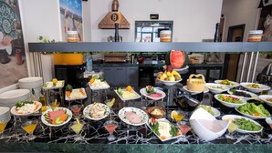 A buffet spread with various food items and drinks, a kitchen area in the background, and a decorative wall with a painting. - Bulton Hotel Airport (Arnavutköy)