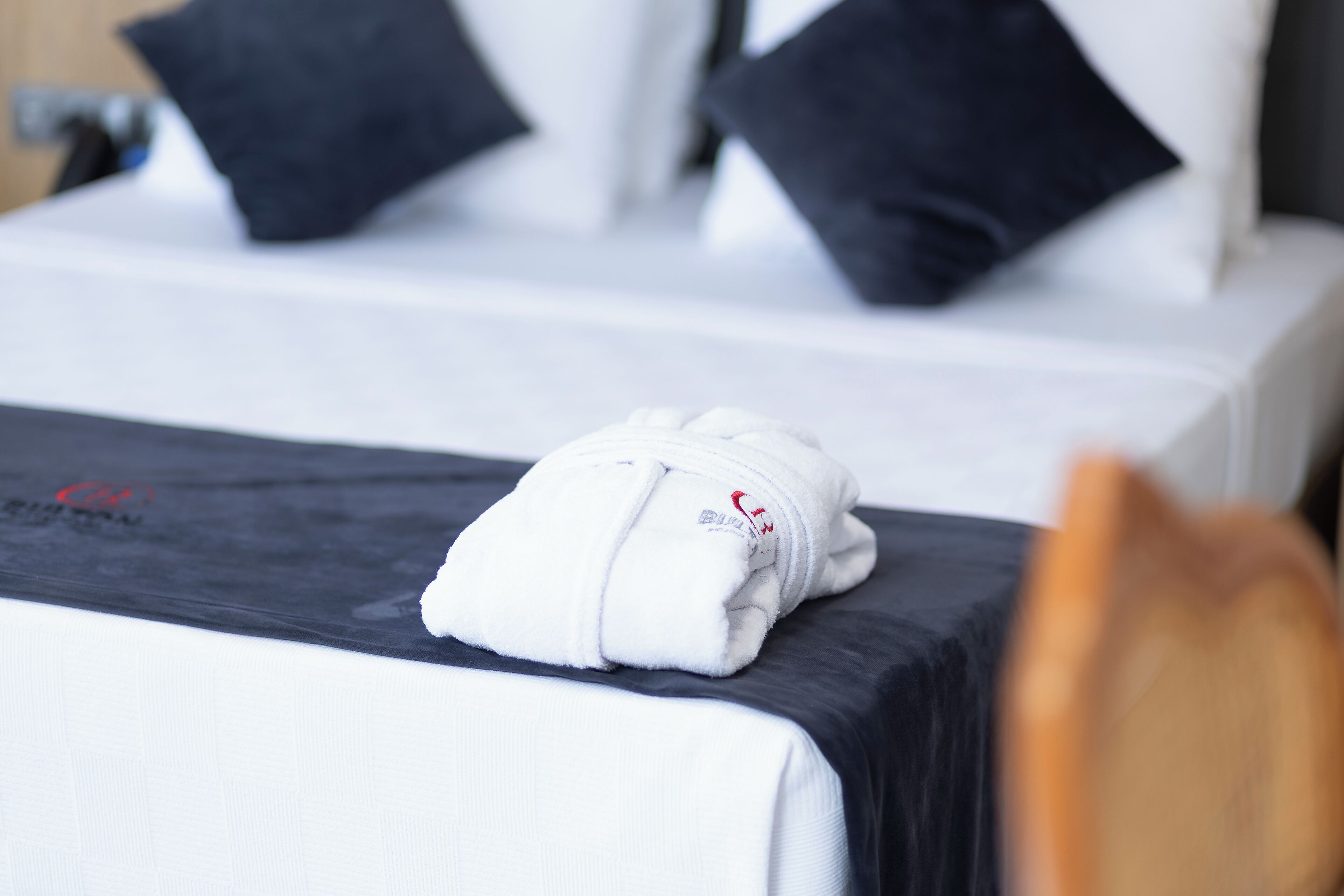 A neatly made bed with white bedding and a folded white towel on the side.