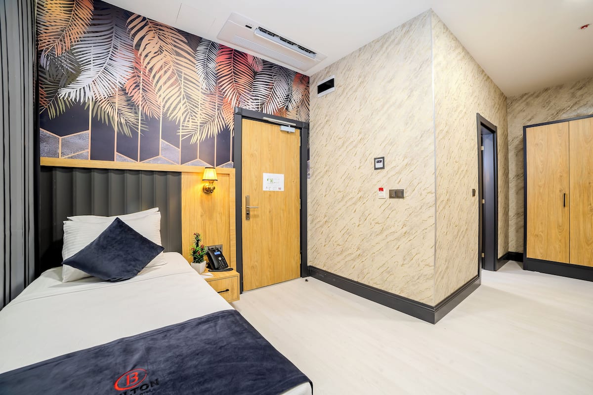 Ein Hotelzimmer mit einem Bett, einem Nachttisch, einem an der Wand montierten Telefon, einer Tür und einem Kleiderschrank.