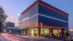 A modern hotel building with a glass facade, illuminated by red and blue lights, and a sign indicating it is the "BULLTON HOTEL." - Bulton Hotel Airport (Arnavutköy)
