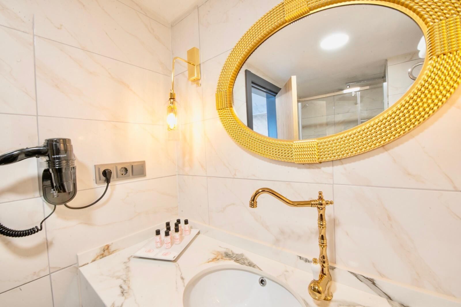 Un baño con lavamanos de mármol, grifo dorado, secador de pelo y espejo con marco dorado.