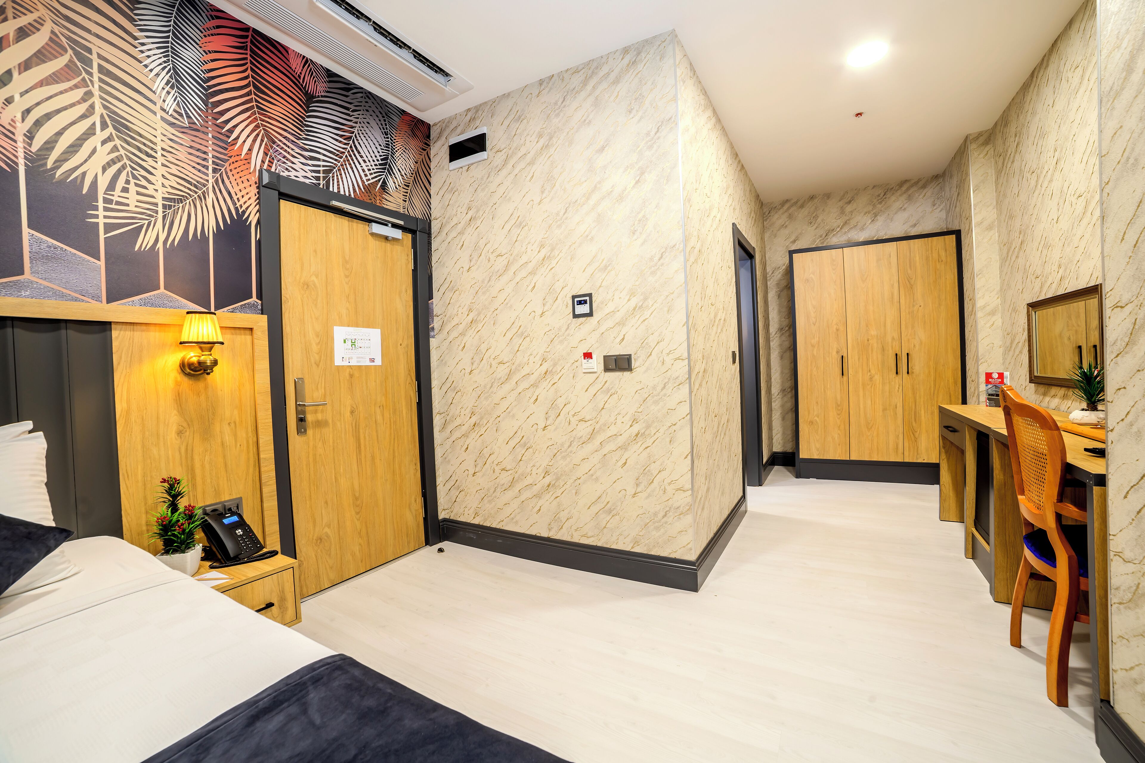 Ein Hotelzimmer mit Bett, Nachttisch mit Lampe, Schreibtisch mit Stuhl und Kleiderschrank.