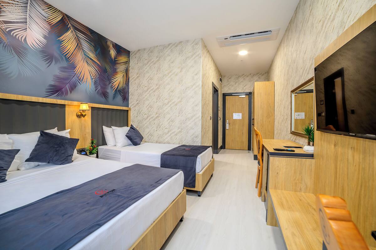 Ein Hotelzimmer mit zwei Betten, einem Schreibtisch, einem Sessel, einem Fernseher und einem großen Wandbild.
