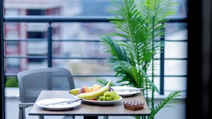 A dining table with plates of fruit, a chair, and a potted plant in a modern setting with a city view. - Bulton Hotel Airport (Arnavutköy)
