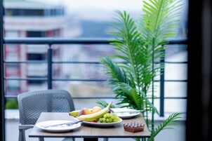 Una mesa de comedor con platos de fruta, una silla y una planta en maceta, todo en un ambiente moderno con vistas a la ciudad.