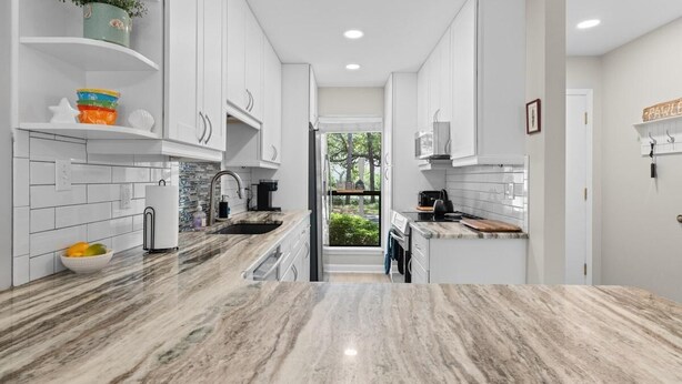 Una cocina moderna con armarios blancos, una encimera de mármol y vistas al exterior.