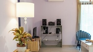 Una sala de estar moderna con una mesa redonda de vidrio, una planta en maceta, un sillón azul, una cafetera y un televisor sobre un mueble de madera.