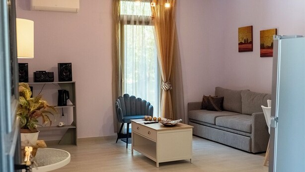 Una sala de estar con sofá, mesa de centro, una silla, una planta y una estantería con altavoces.