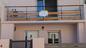 Een gebouw met twee verdiepingen, een balkon, een houten hek en een bord dat een locatie aangeeft.