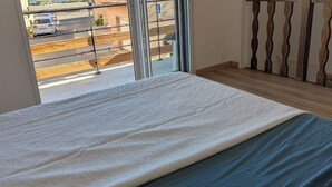Een kamer met een bed, uitzicht op een straat door een raam, en een houten vloer.