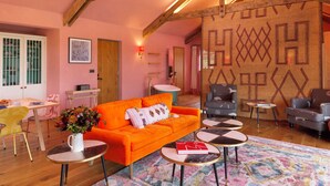 Un salon chaleureux avec un canapé orange vif, des poutres en bois, un mur à motifs et un plancher en bois.