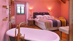 Une chambre avec un grand lit, un plafond en bois, une fenêtre avec des rideaux, une table de chevet avec une lampe et une baignoire.
