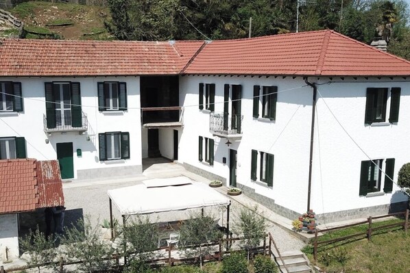 Un edificio blanco con tejados de tejas rojas y contraventanas verdes, con un patio central que incluye una mesa y sillas.