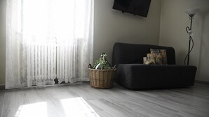 Una sala de estar con un sofá oscuro, una cesta de mimbre con una planta y una lámpara.