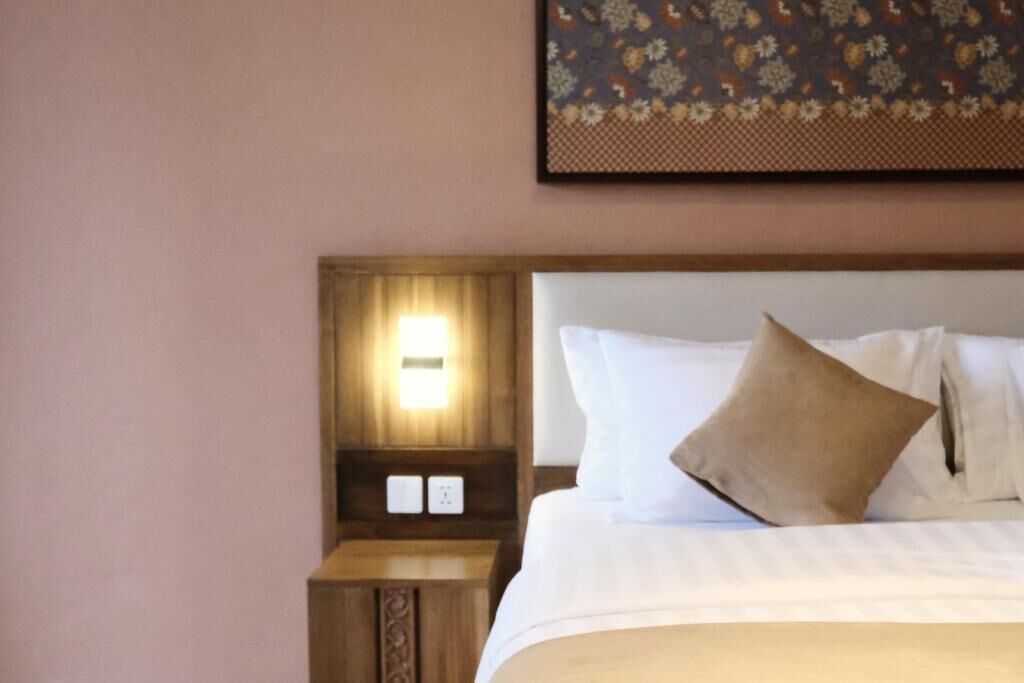 A hotel room with a wooden headboard, a bedside lamp, and a bed with white linens and a brown pillow.