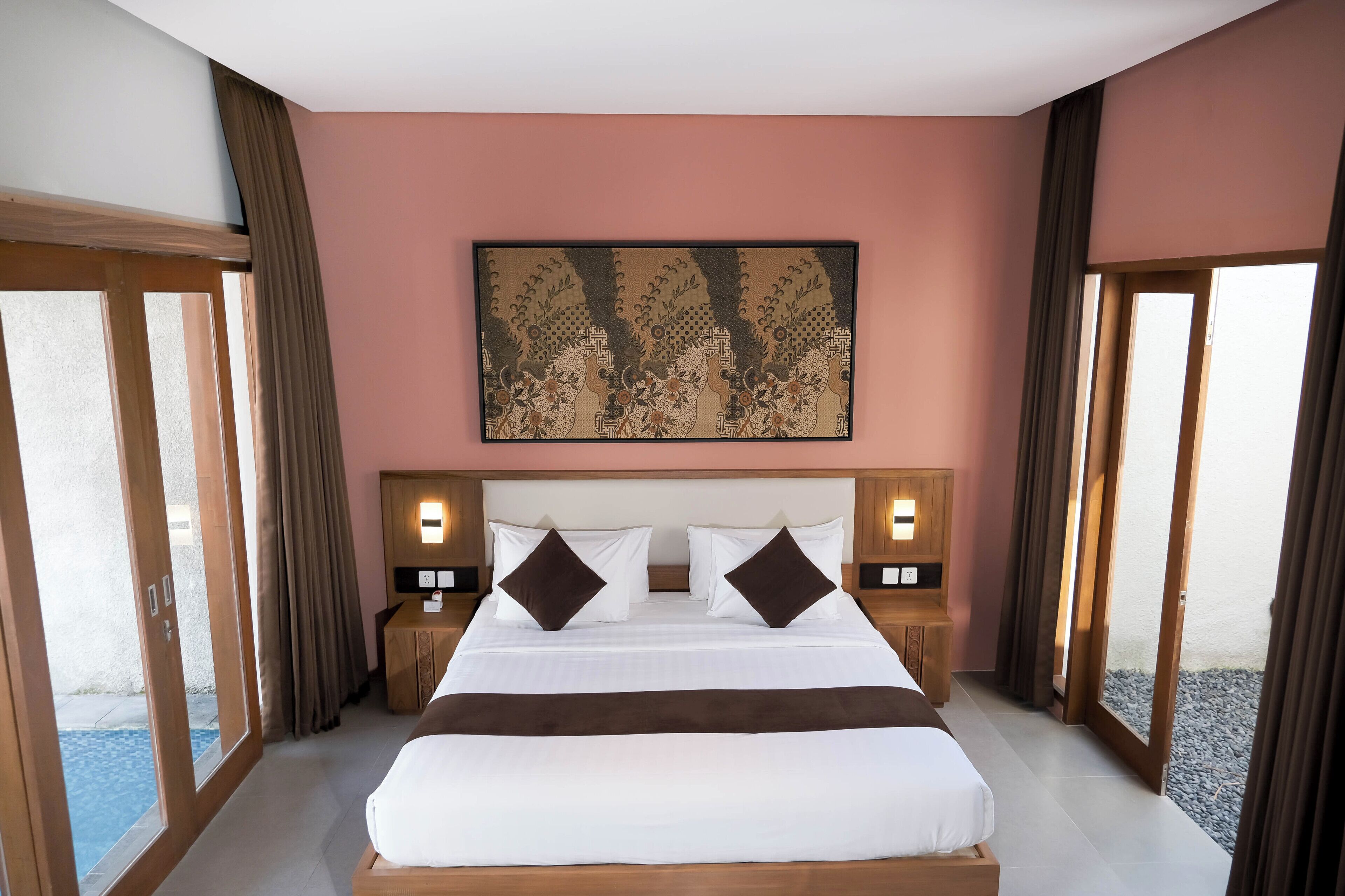 A hotel room with a large bed, two nightstands, a wall-mounted artwork, and a view through the glass doors.