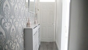 Un couloir étroit avec un papier peint à motifs, une commode blanche et une porte.
