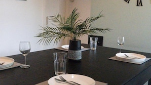 Une table à manger dressée avec des assiettes, des couverts et des verres, agrémentée d’une plante en pot et d’un vase décoratif.