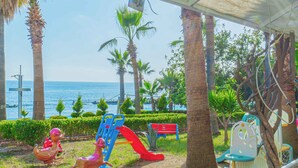 A covered outdoor area with a slide, seating, and palm trees. - Pyxis Point Hotel - All Inclusive (Alanya)