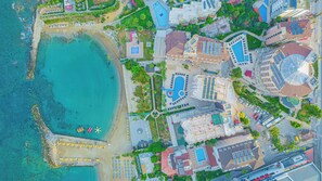 An aerial view of a coastal resort with a beach, swimming pools, and various buildings.