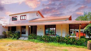 Une maison à deux étages, avec un toit en tuiles, un porche et un petit jardin.