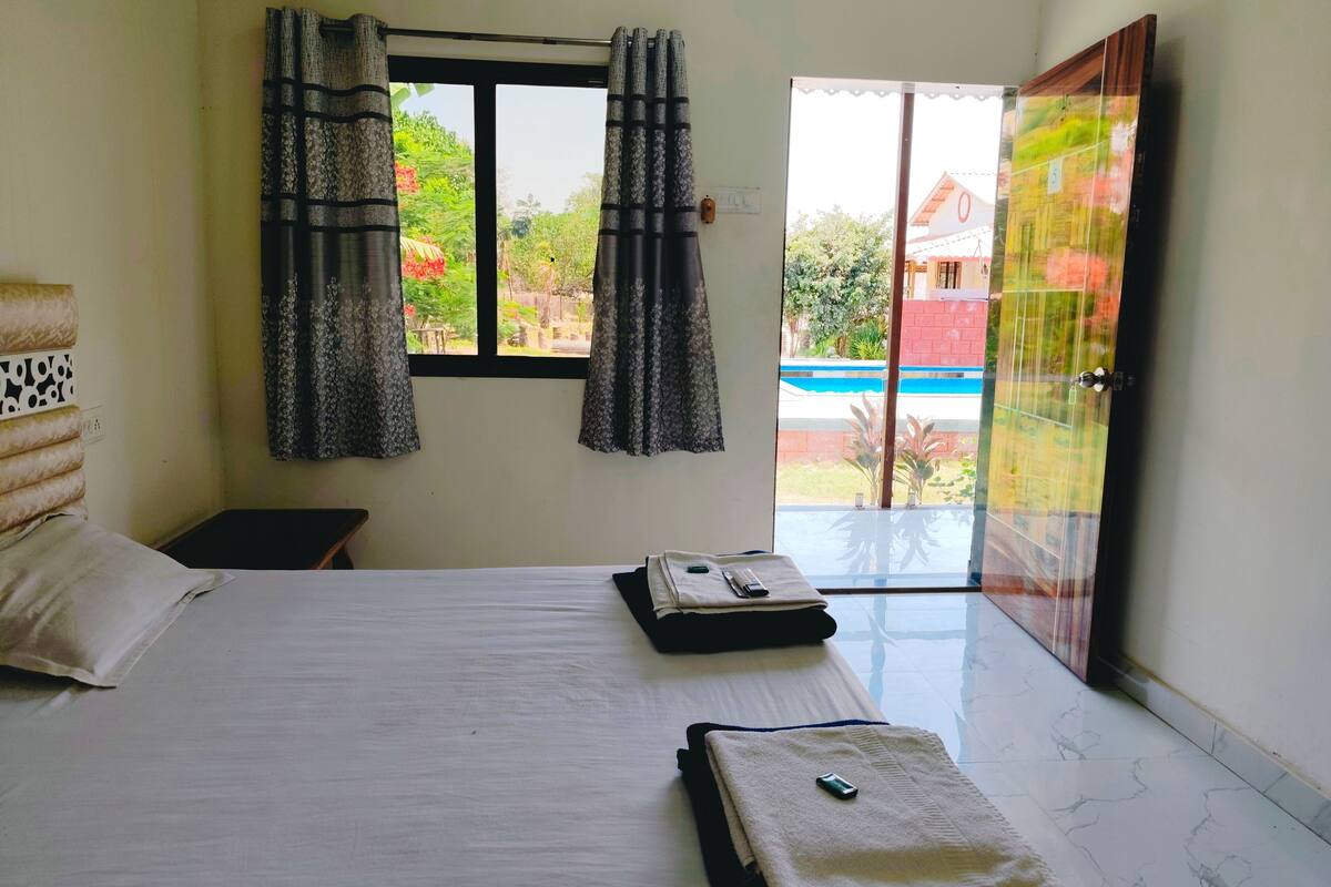 Quarto de hotel com cama, uma mesinha, janela com cortinas e vista para o exterior.