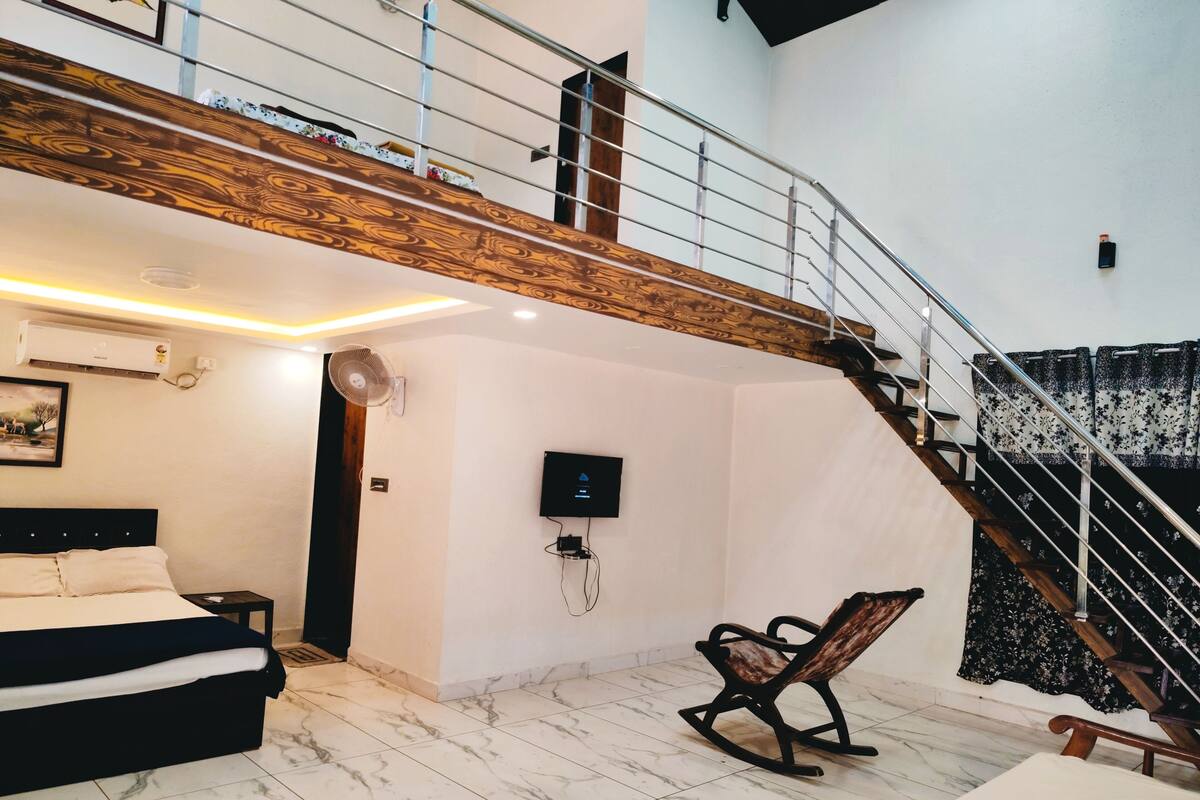 Quarto com cama, teto de madeira, televisão e escada.