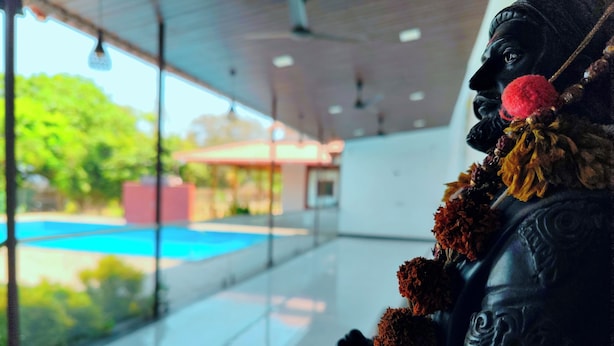 Une statue ornée d’une guirlande, un mur de verre et une vue sur une piscine et des arbres.