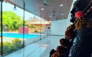 Une statue ornée d’une guirlande, un mur de verre et une vue sur une piscine et des arbres.