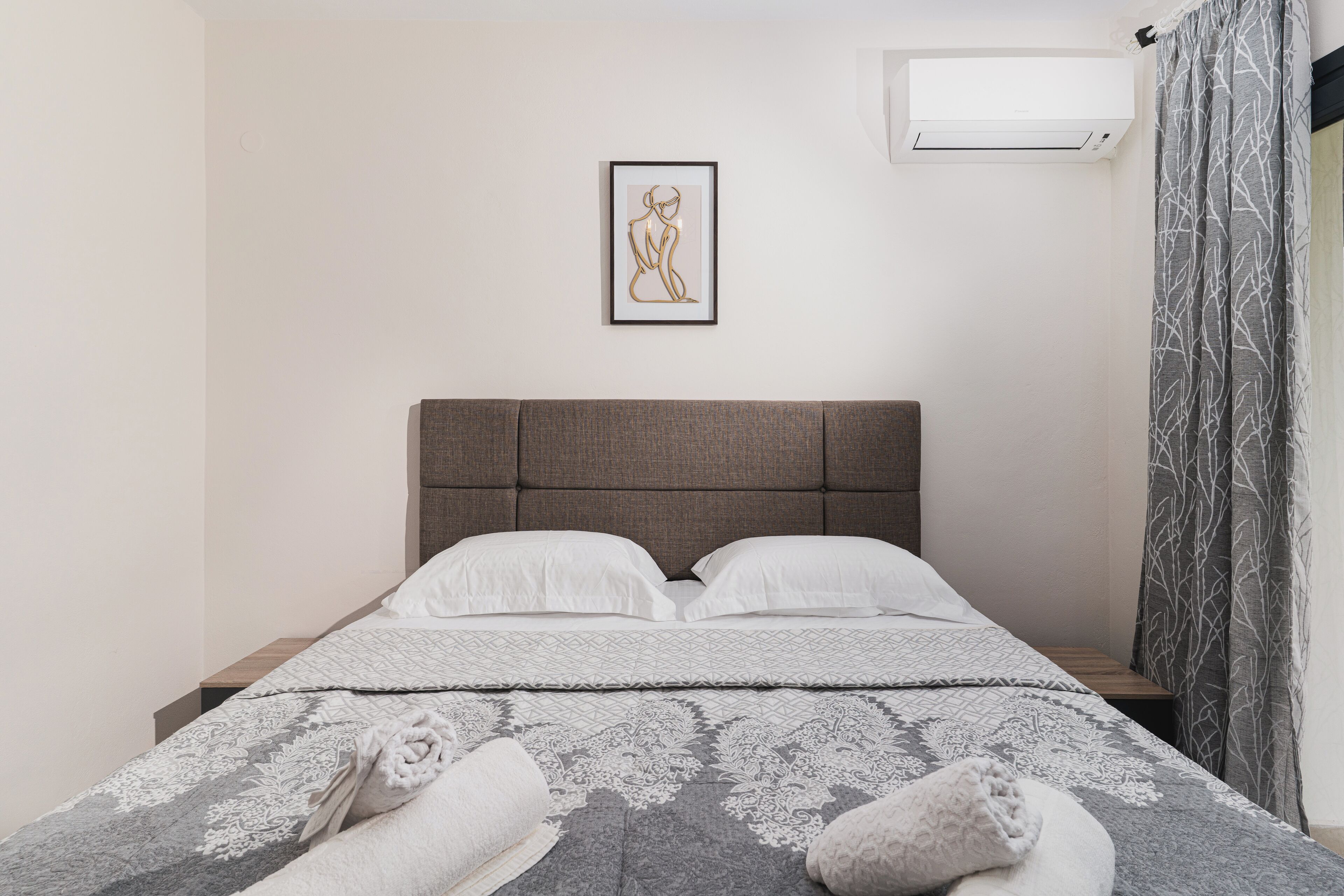 Un lit bien fait, avec une couette à motifs gris et blancs, deux oreillers blancs et une tête de lit grise.