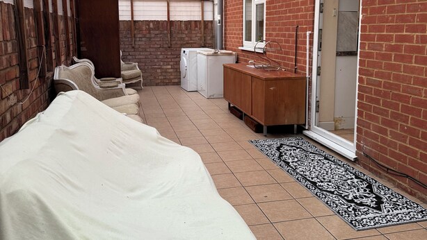 Een overdekt terras met een bed, een wasmachine en een houten kast.