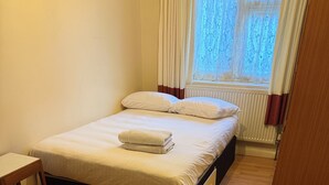 Een slaapkamer met een bed, een houten vloer, een nachtkastje en een raam met gordijnen.