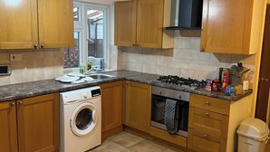 Een keuken met houten kastjes, een wasmachine, een fornuis en een vuilnisbak.