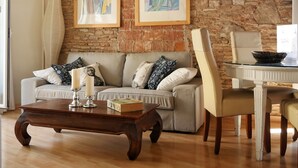 A living room with a brick wall, a sofa, a coffee table, and a dining area with a chair and table. - Stay U-nique Apartments Monec (Barcelona)