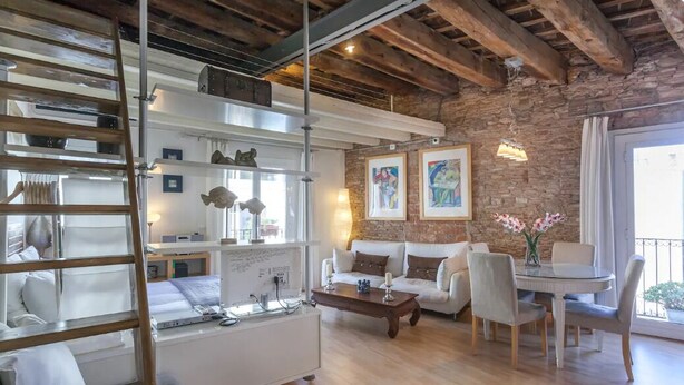 A modern living room with a sofa, a dining table, and a ladder. There are framed pictures on the wall and a window with curtains. - Stay U-nique Apartments Monec (Barcelona)