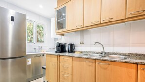 A modern kitchen with stainless steel appliances, wooden cabinets, a granite countertop, and a window providing natural light.